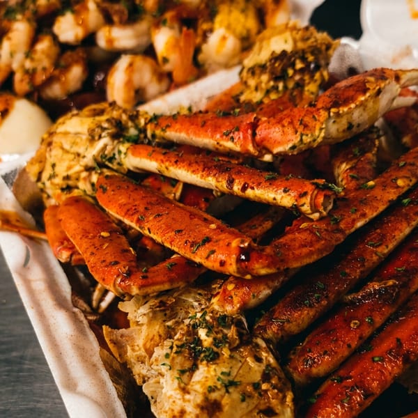 Spicy seasoned crab legs and shrimp in white takeout containers.