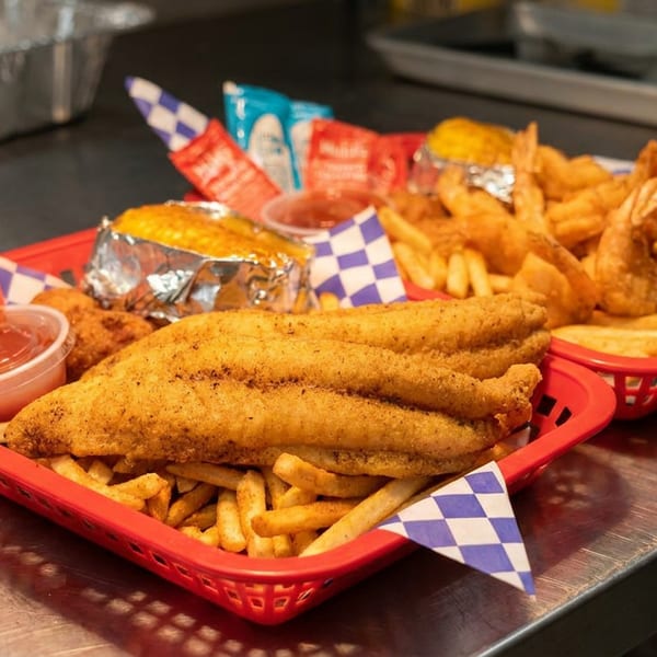 Crispy fried fish, shrimp, french fries, and corn on the cob served in red baskets.