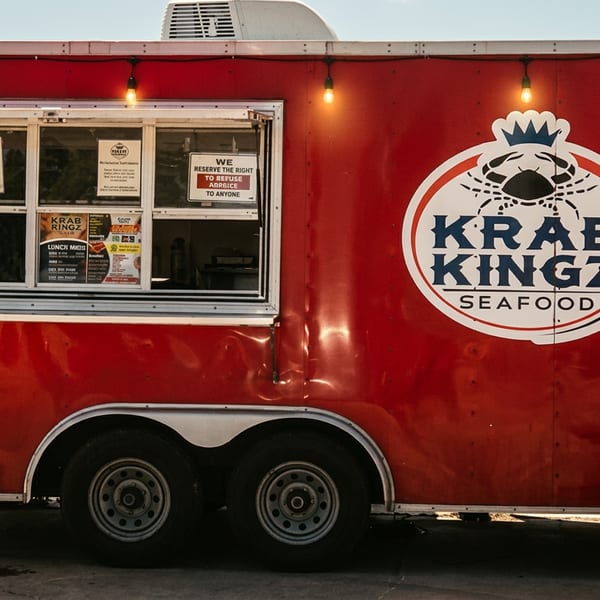 Red Krab Kingz Seafood food truck with a serving window, string lights, and a red picnic table.