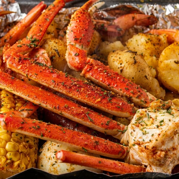 A vibrant seafood boil with seasoned crab legs, corn, potatoes, and shrimp in a foil container.