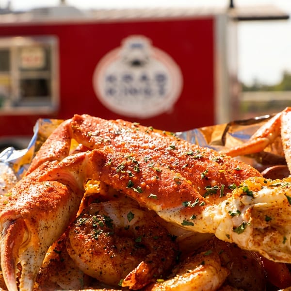 Seasoned crab legs and seafood boil in foil, with a red food truck in the background.