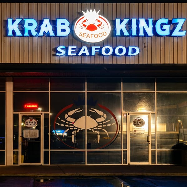 Illuminated Krab Kingz Seafood restaurant exterior at night with blue neon sign and crab window decals.