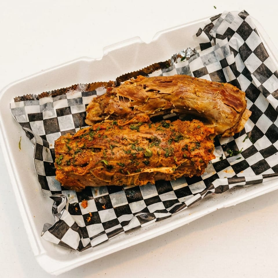 Two pieces of seasoned meat, one shredded, in a white takeout container with checkered paper.